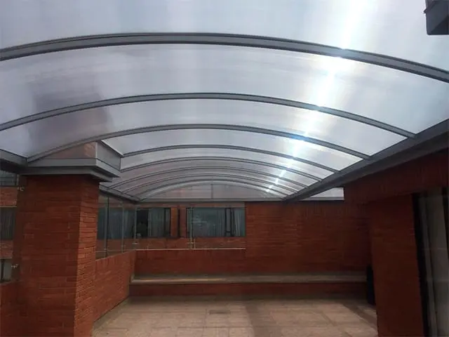 Marquesina curva amplia de policarbonato instalada sobre un patio