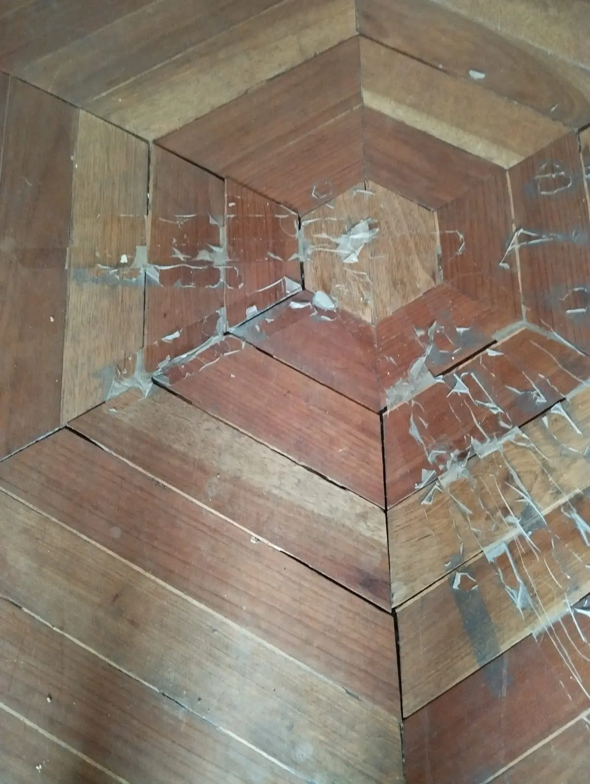 Piso de madera con diseño geométrico antes de la restauración, con desgaste y residuos visibles